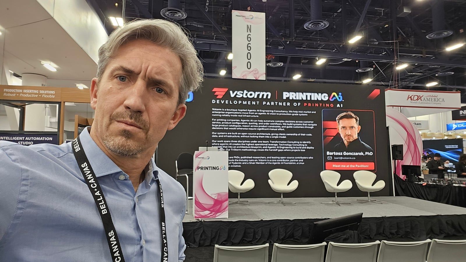 Bartosz Gonczarek at the Vstorm and PRINTING AI pavilion stage at PRINTING United Expo, booth N6600, with the panel chairs set up behind him