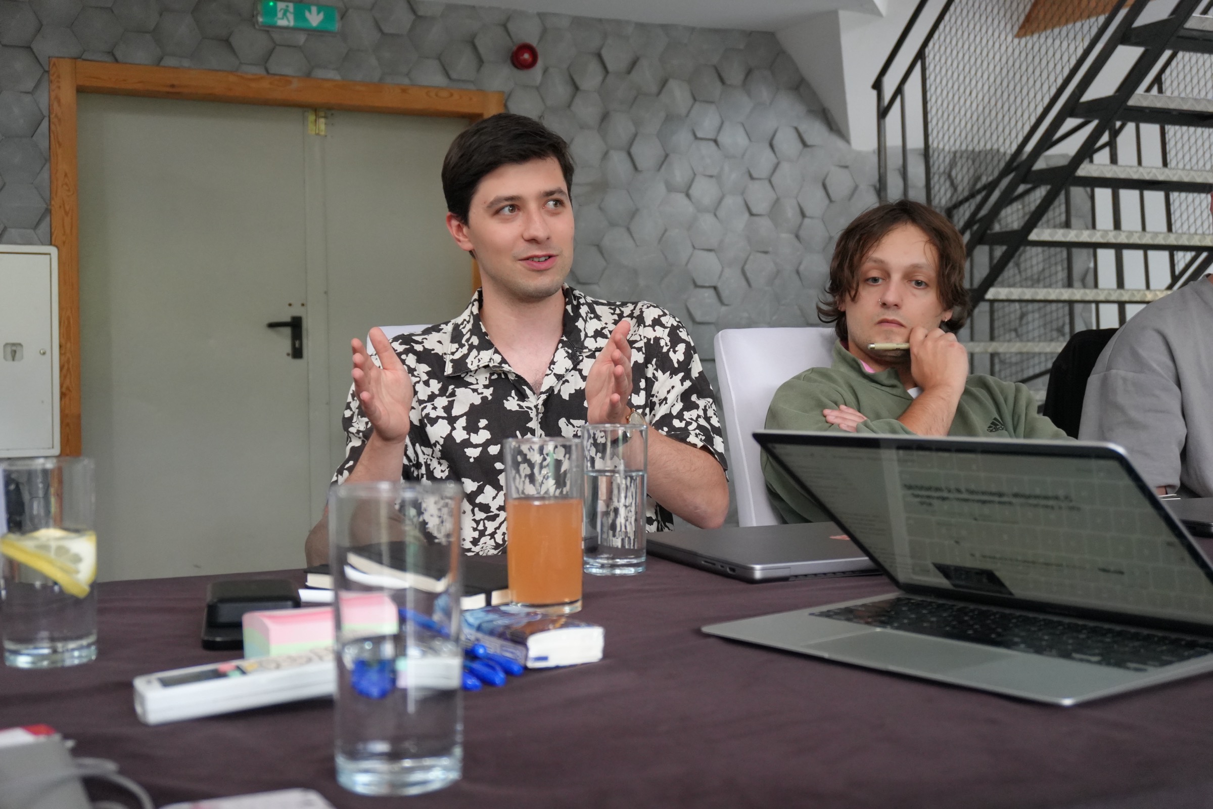 Two Vstorm colleagues at an offsite working session, one explaining at an open laptop on a conference table