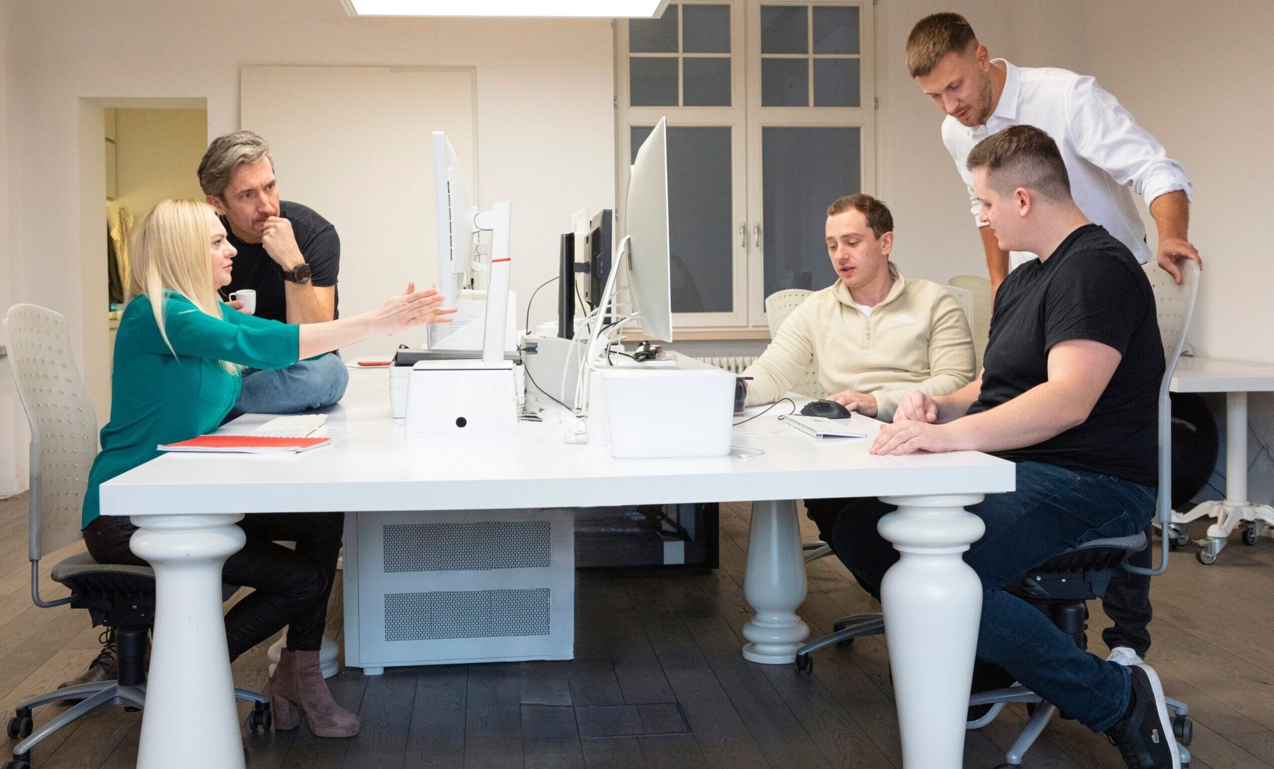 Five Vstorm colleagues working together at white desks in the office, two at monitors and three talking